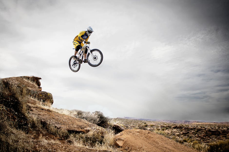 A cyclist performs a daring jump off a rocky cliff under a cloudy sky
